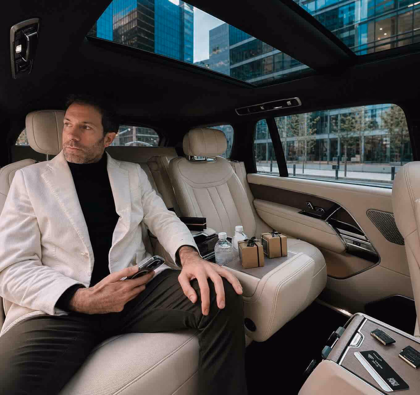 Passeggero seduto nei sedili posteriori di un SUV premium con interni chiari, tetto panoramico e comfort executive.