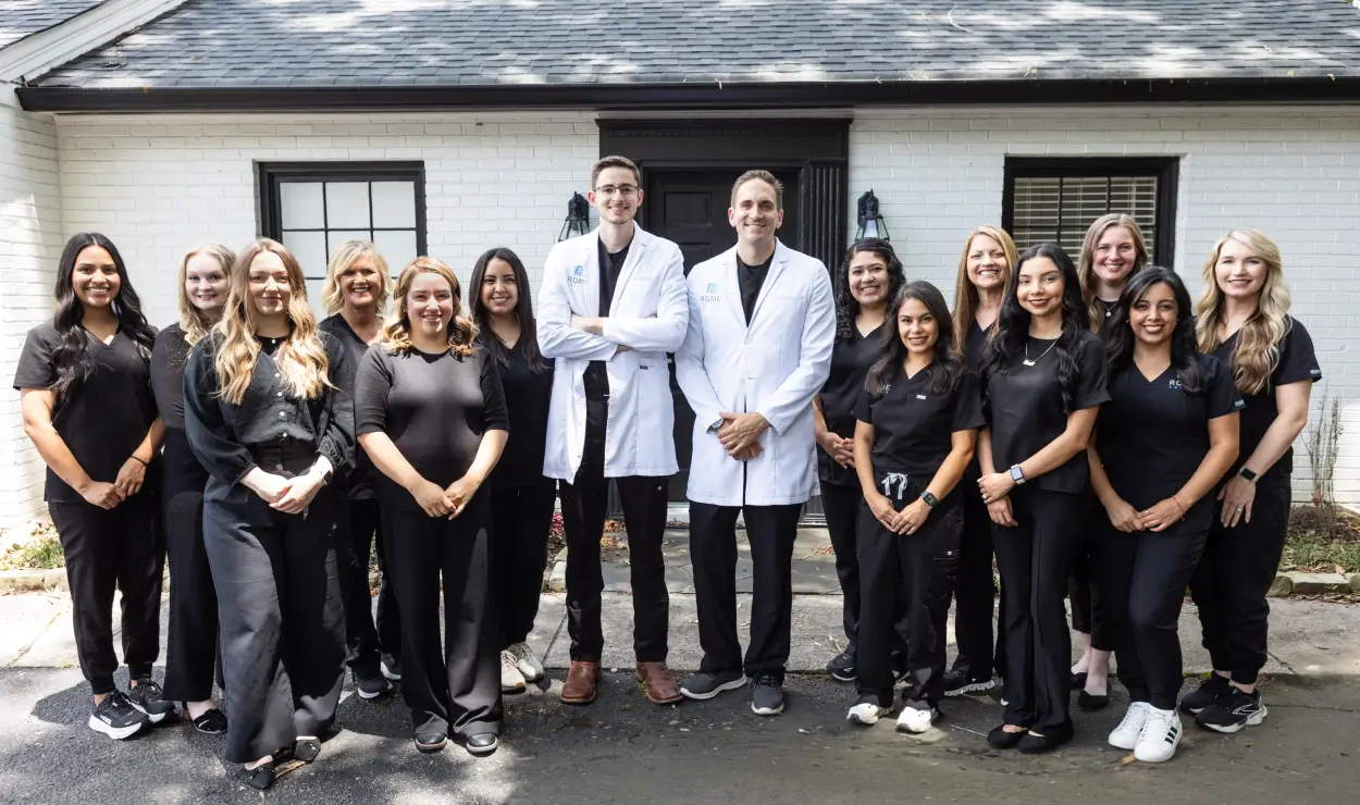Two doctors in white coats stand with a team of staff in black uniforms outside a building.