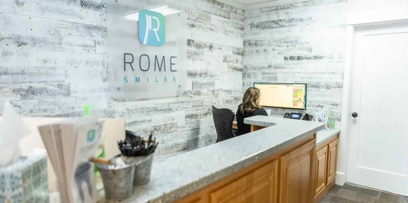A woman works at a computer behind the reception desk in a dental office.