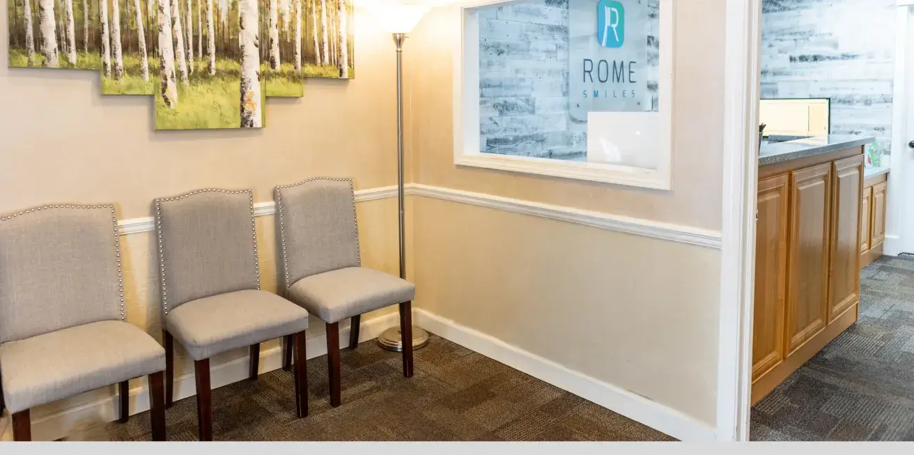Three grey chairs are lined up next to a standing lamp in a waiting area.