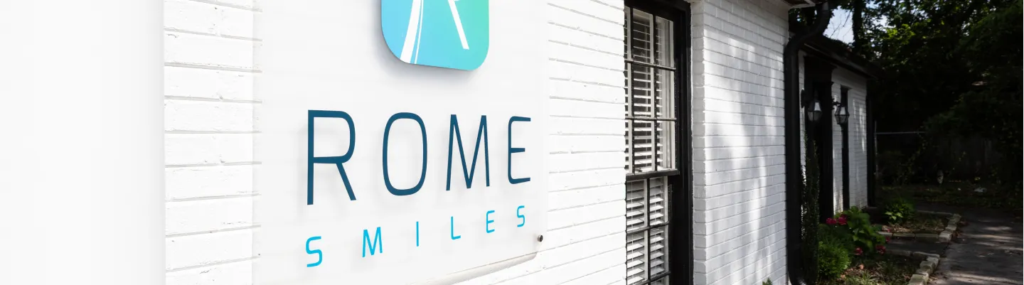 Sign on a white brick building reads "Rome Smiles" with a blue dental logo above.