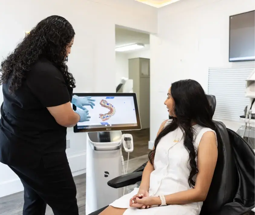 A dental professional shows a patient something on a screen while the patient sits in a chair.