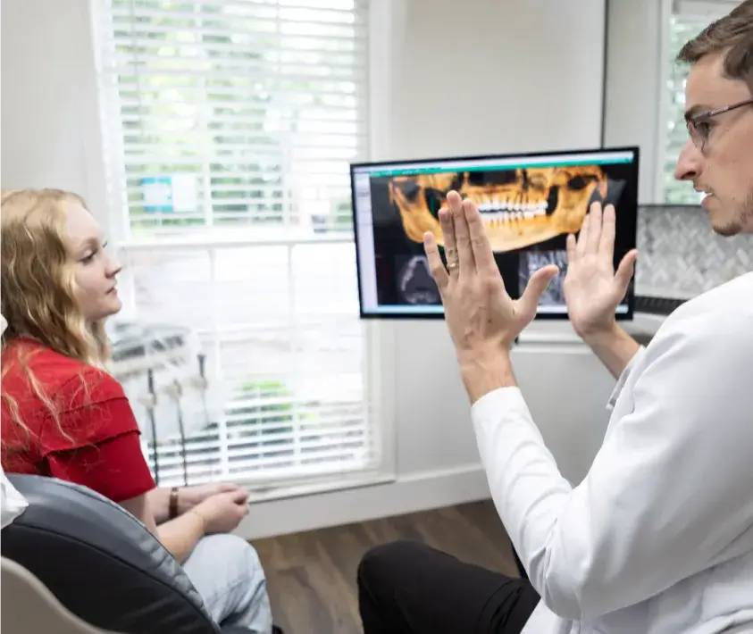 A dentist explains dental images on a screen to a patient sitting in the office.