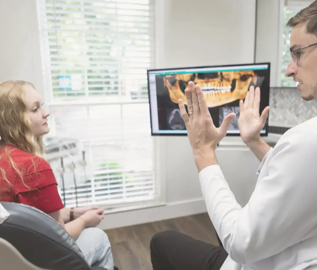 Dentist explains a dental X-ray to a patient in an examination room.