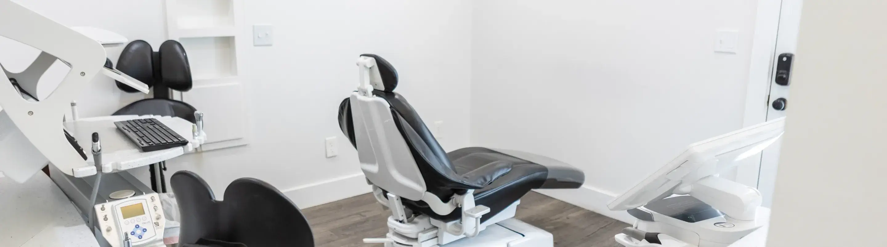 A clean, modern dental exam room with two black dental chairs and a computer workstation.