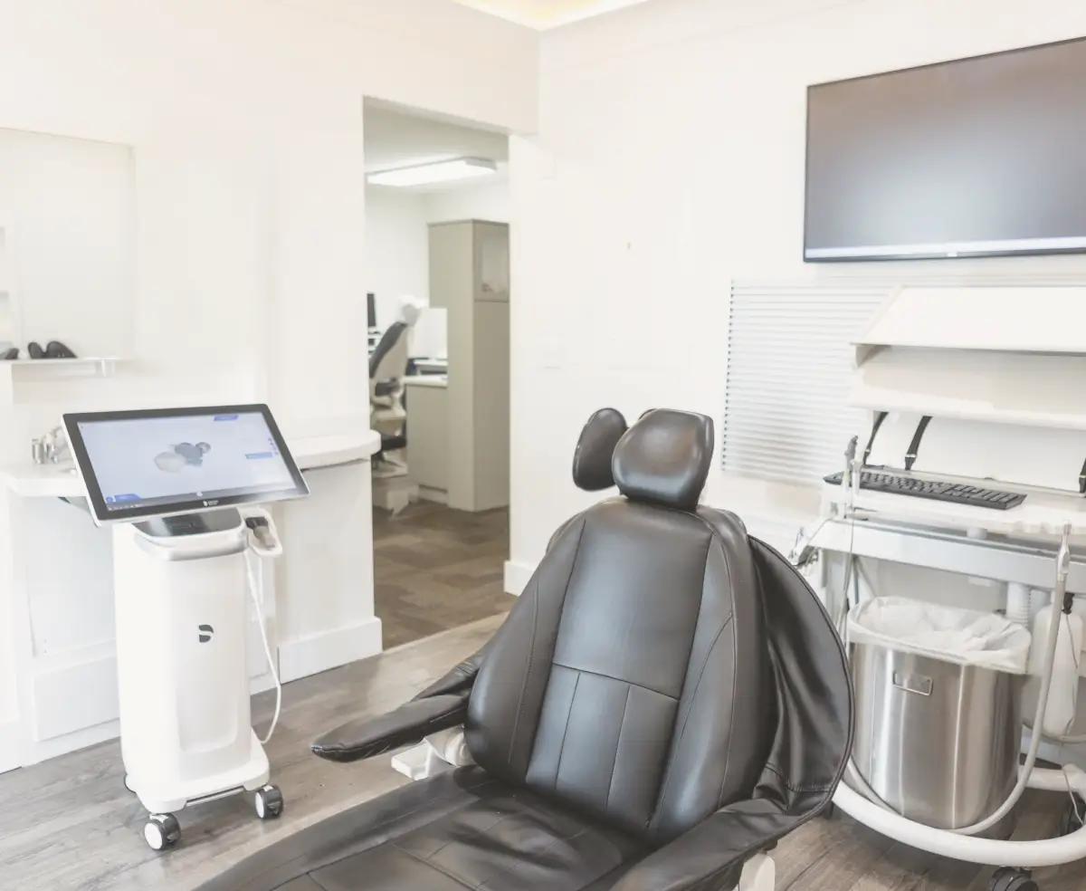 A black dental chair in a modern, white dental office with a screen and equipment.