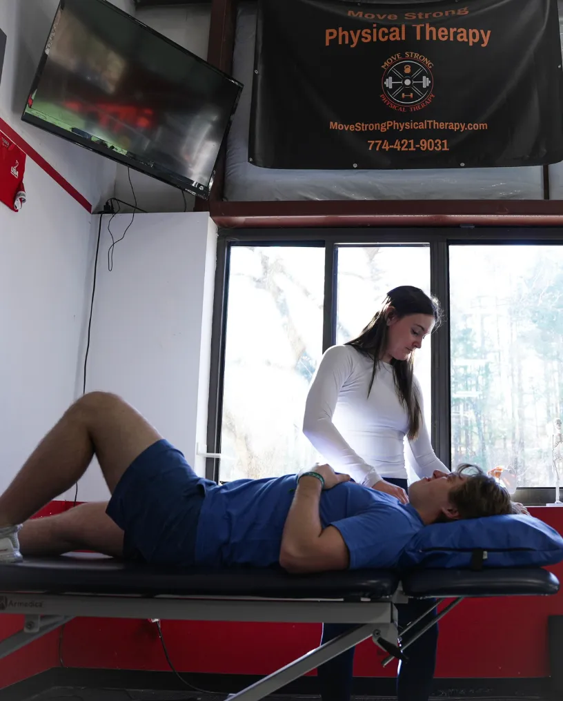 Physical therapist evaluating a male patient lying on a treatment table inside a therapy clinic.