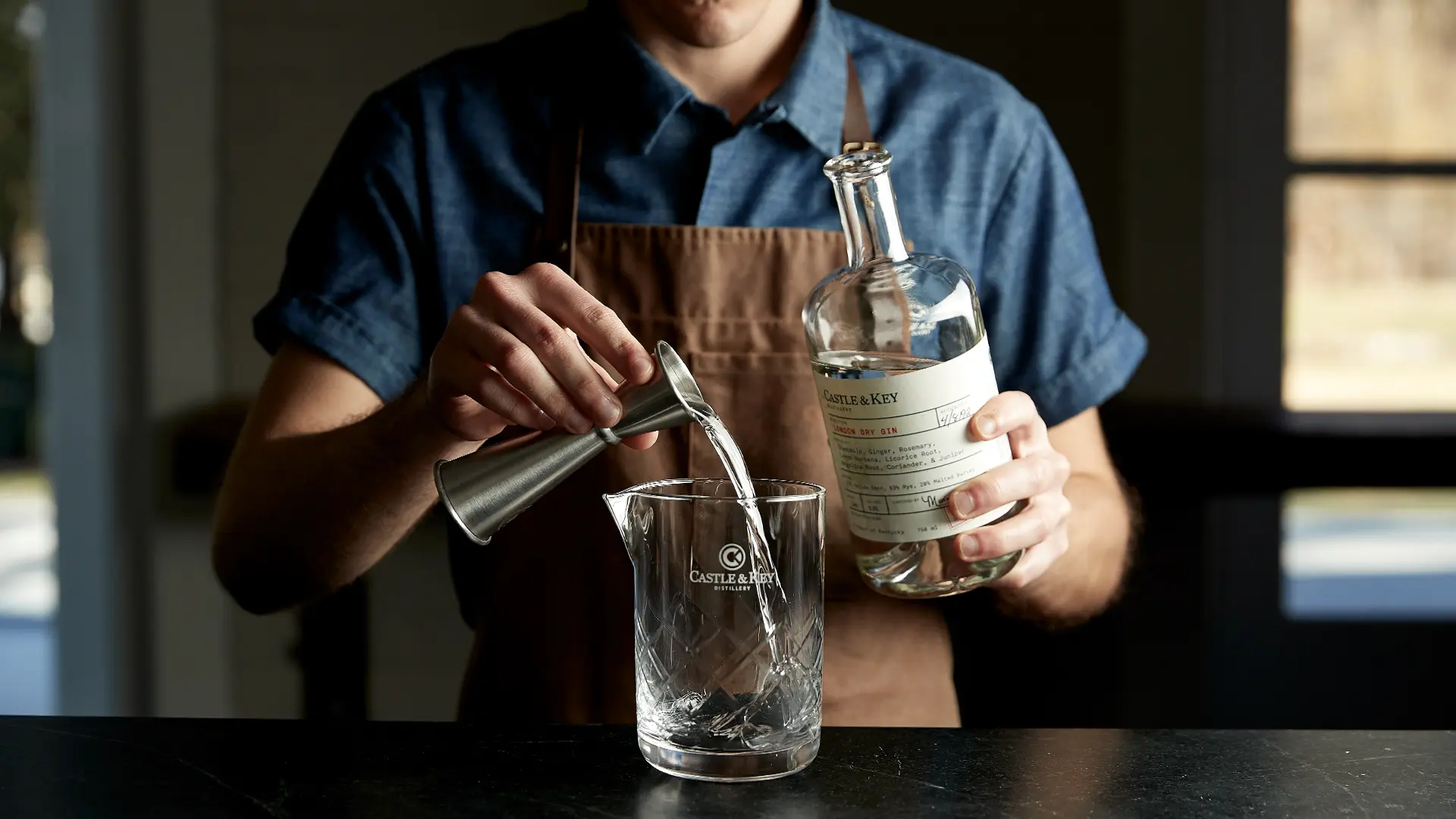 Image of a person, shown carefully pouring a glass of Castle & Key gin.