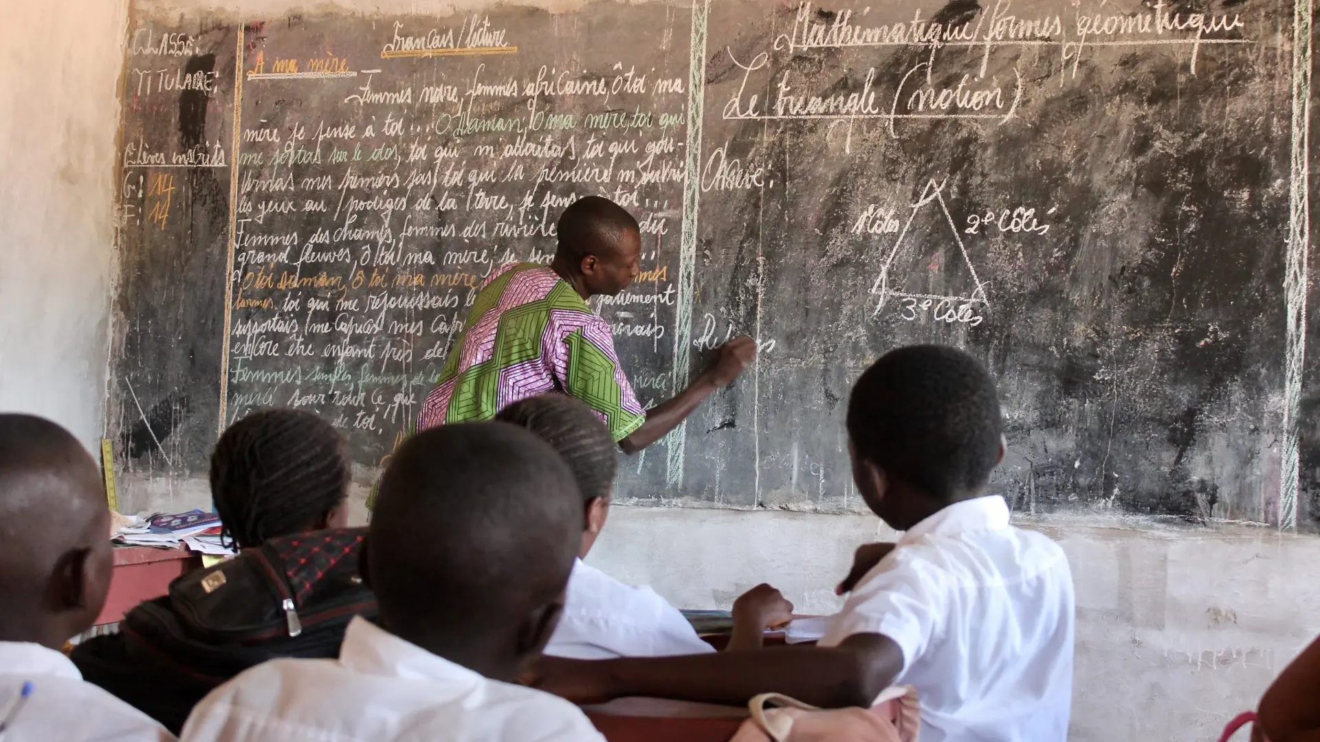 An instructor writing on a chalkboard in front of a classroom of students