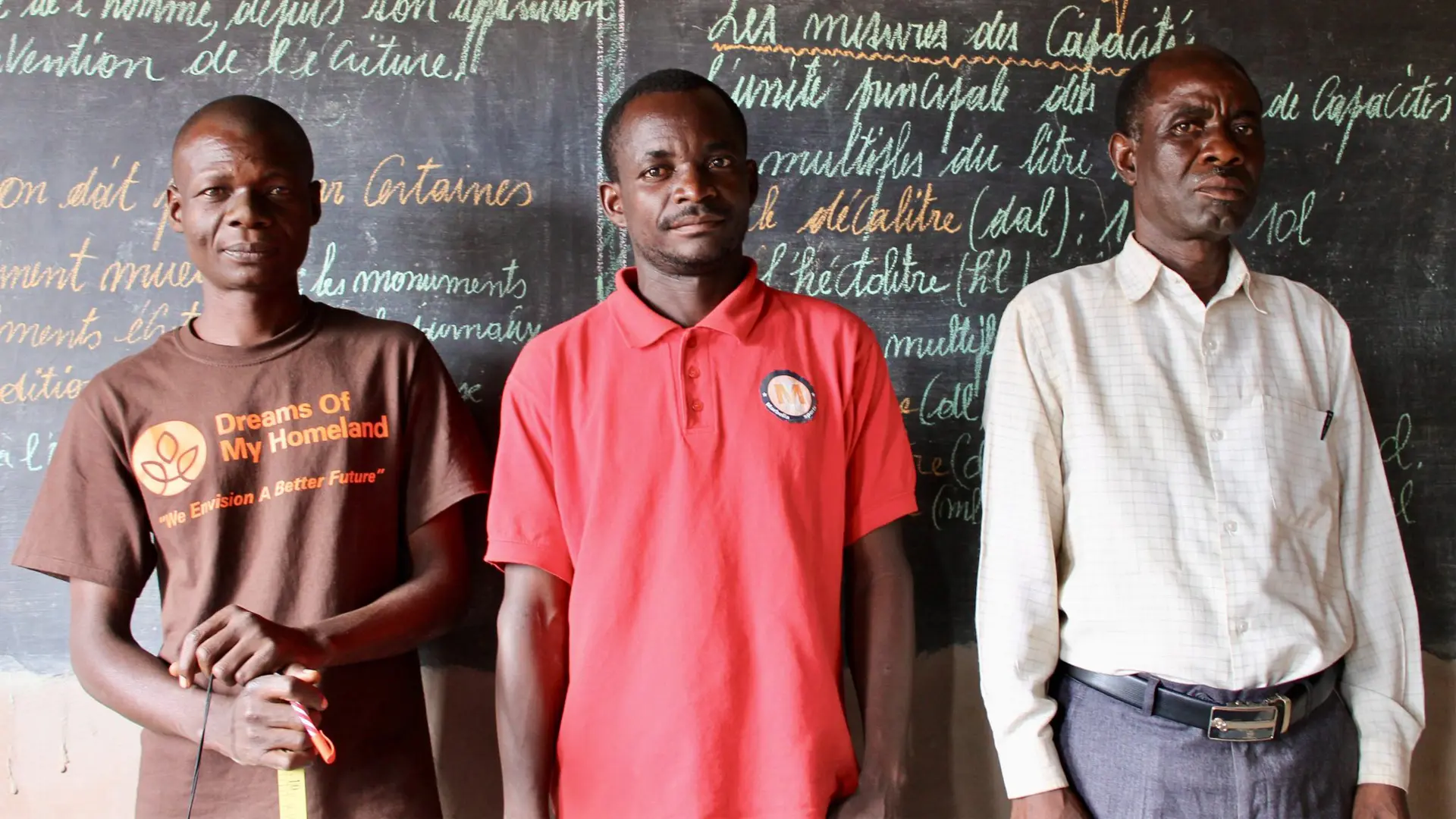 Three men standing in front of a chalkboard at a school