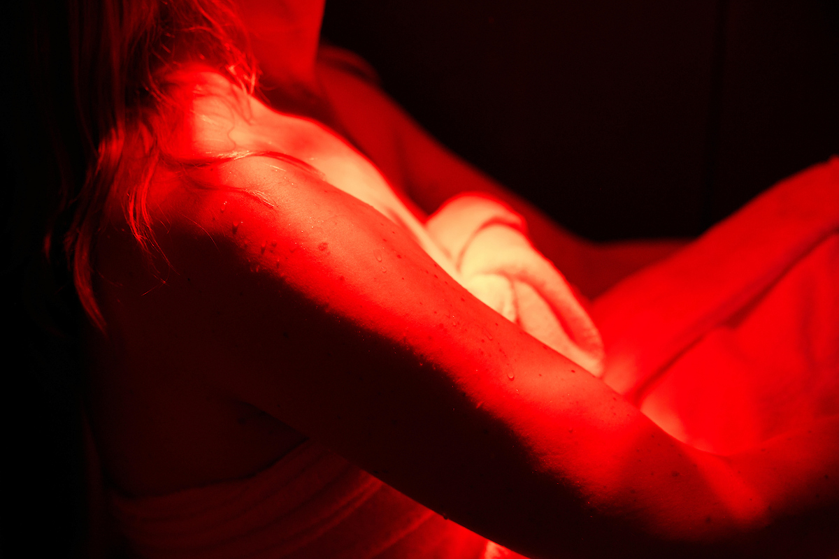 Close-up of a person's upper arm and shoulder illuminated by intense red light, with visible water droplets on the skin.