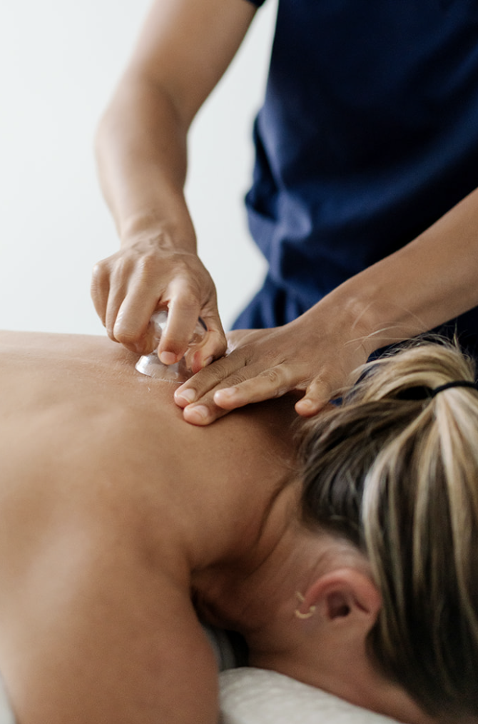 Person receiving a cupping therapy massage on their upper back while lying face down, with the therapist pressing a glass cup on the skin.
