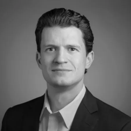 Black and white headshot of a man with short dark hair wearing a dark blazer and light shirt.