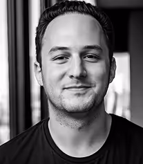 Black and white portrait of a smiling man with short dark hair wearing a dark shirt.