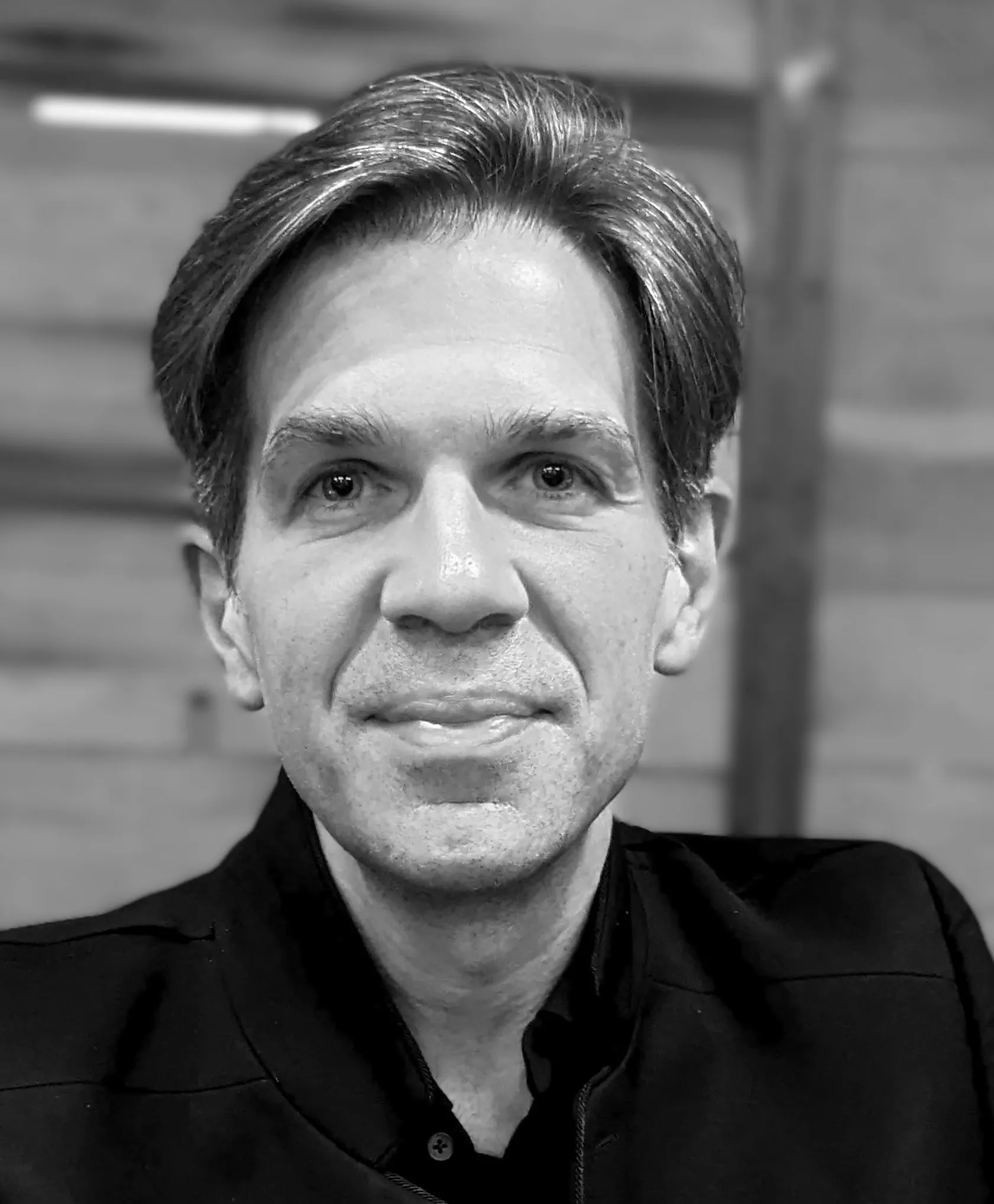 Black and white close-up portrait of a middle-aged man with combed-back hair wearing a dark jacket.