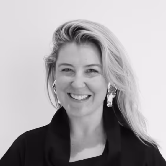Smiling woman with long blond hair wearing large earrings and a black top against a plain background.