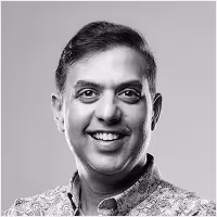 Black and white portrait of a smiling middle-aged man with short dark hair wearing a patterned shirt.