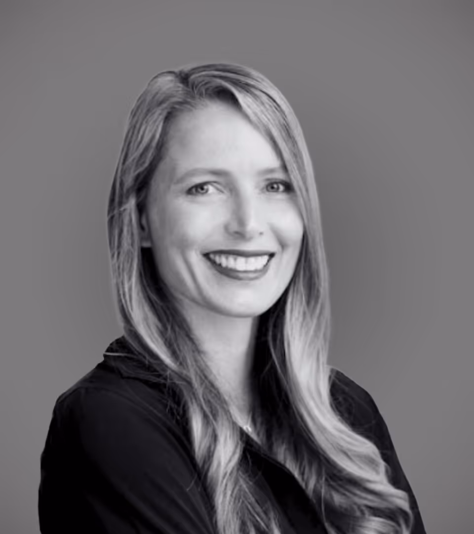 Smiling woman with long, wavy hair wearing a dark top against a plain background.