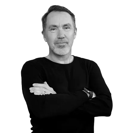 Middle-aged man with short hair and beard, wearing a black long-sleeve shirt and watch, arms crossed, looking at camera.