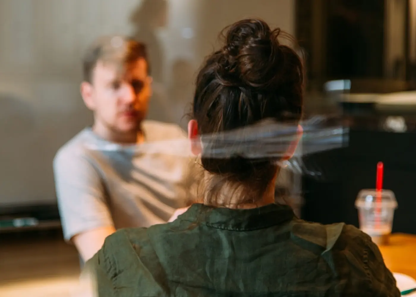 Two people having a conversation indoors, with one person facing the camera and the other seen from the back.