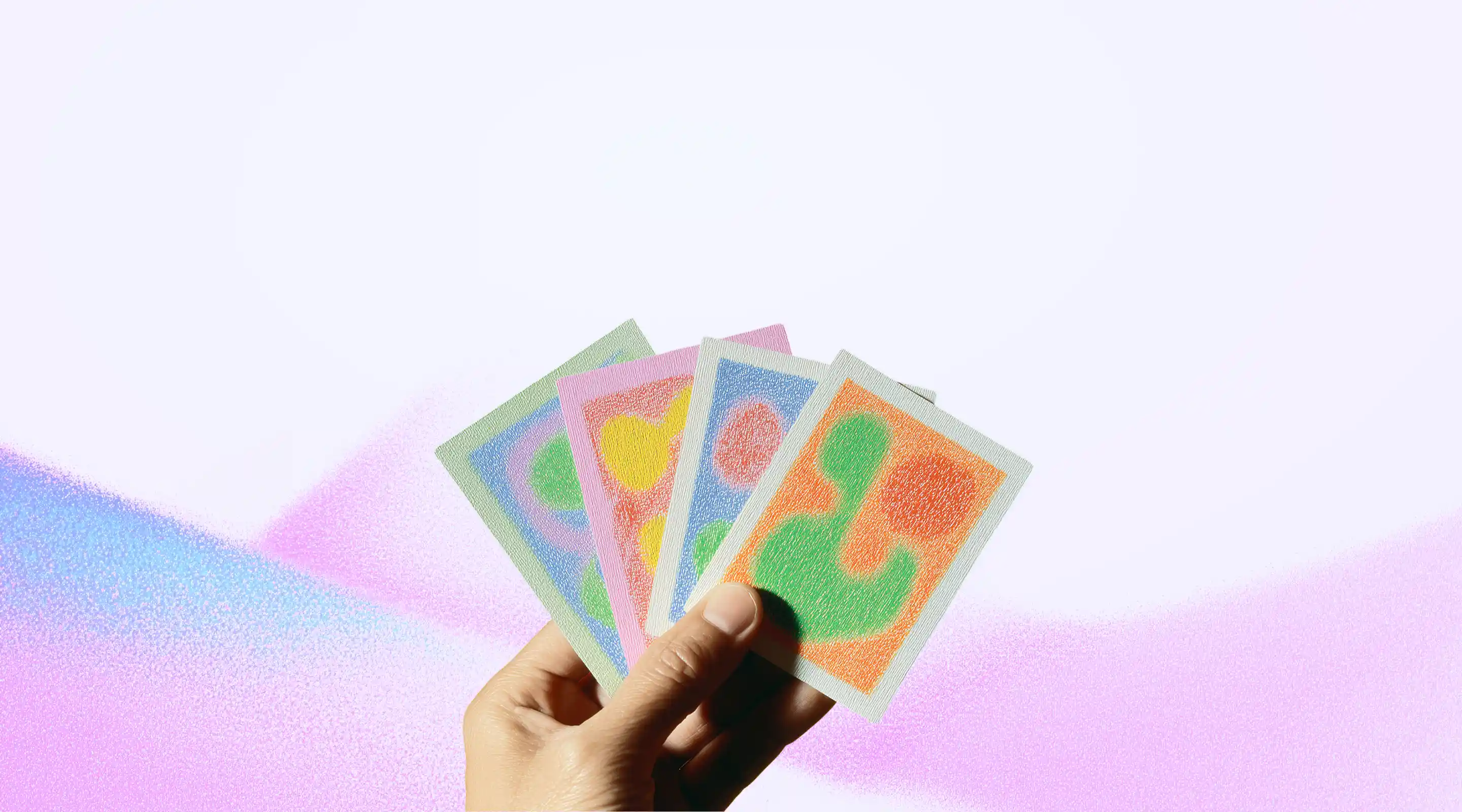 Hand holding four rectangular cards with colorful abstract patterns against a white and pink gradient background.
