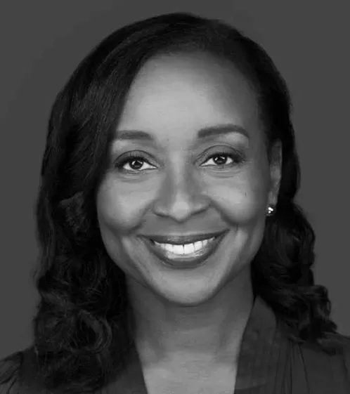 Black and white headshot of a smiling woman with shoulder-length wavy hair and earrings, wearing a collared top.