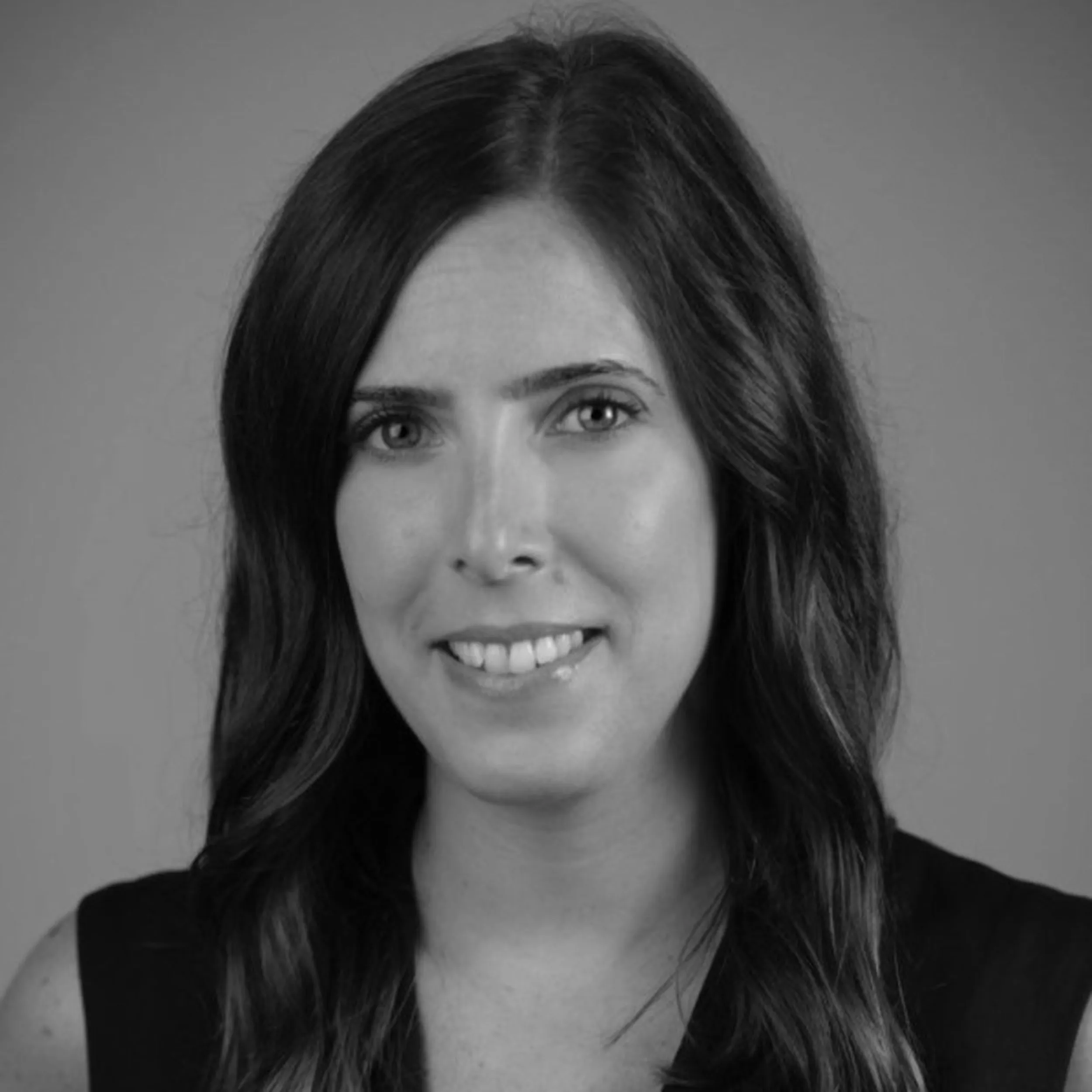 Black and white headshot of a smiling woman with long, wavy dark hair wearing a sleeveless top.