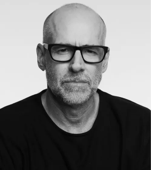 Black and white headshot of a middle-aged man with glasses, a short beard, and a serious expression wearing a black shirt.