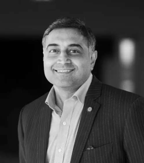 Black and white portrait of a smiling man wearing a pinstripe suit jacket and collared shirt against a blurred background.