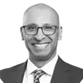 Smiling bald man wearing glasses, a suit, and a tie, posing against a white background.