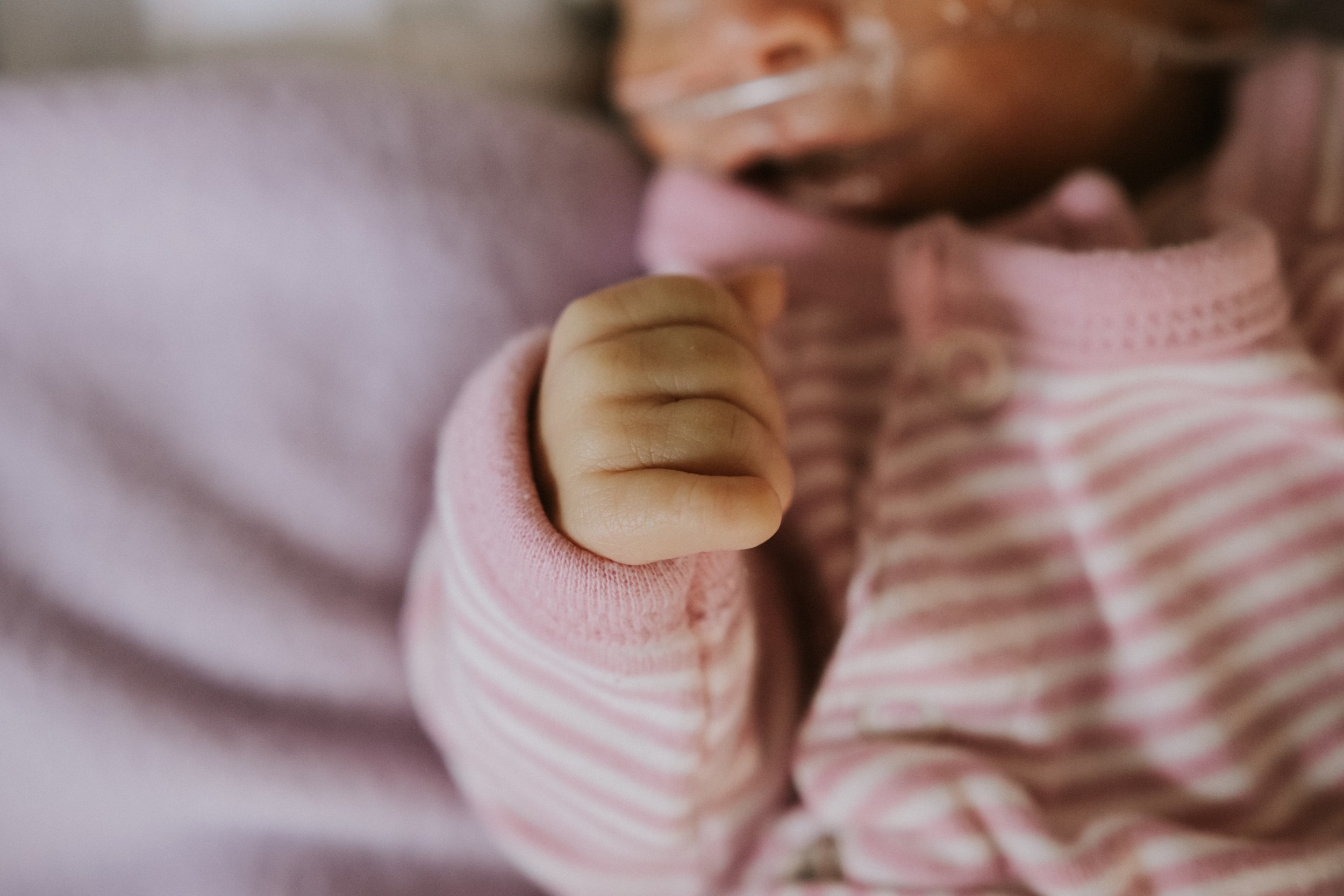 Close-up of a baby's hand clenched into a fist, wearing a pink and white striped outfit.