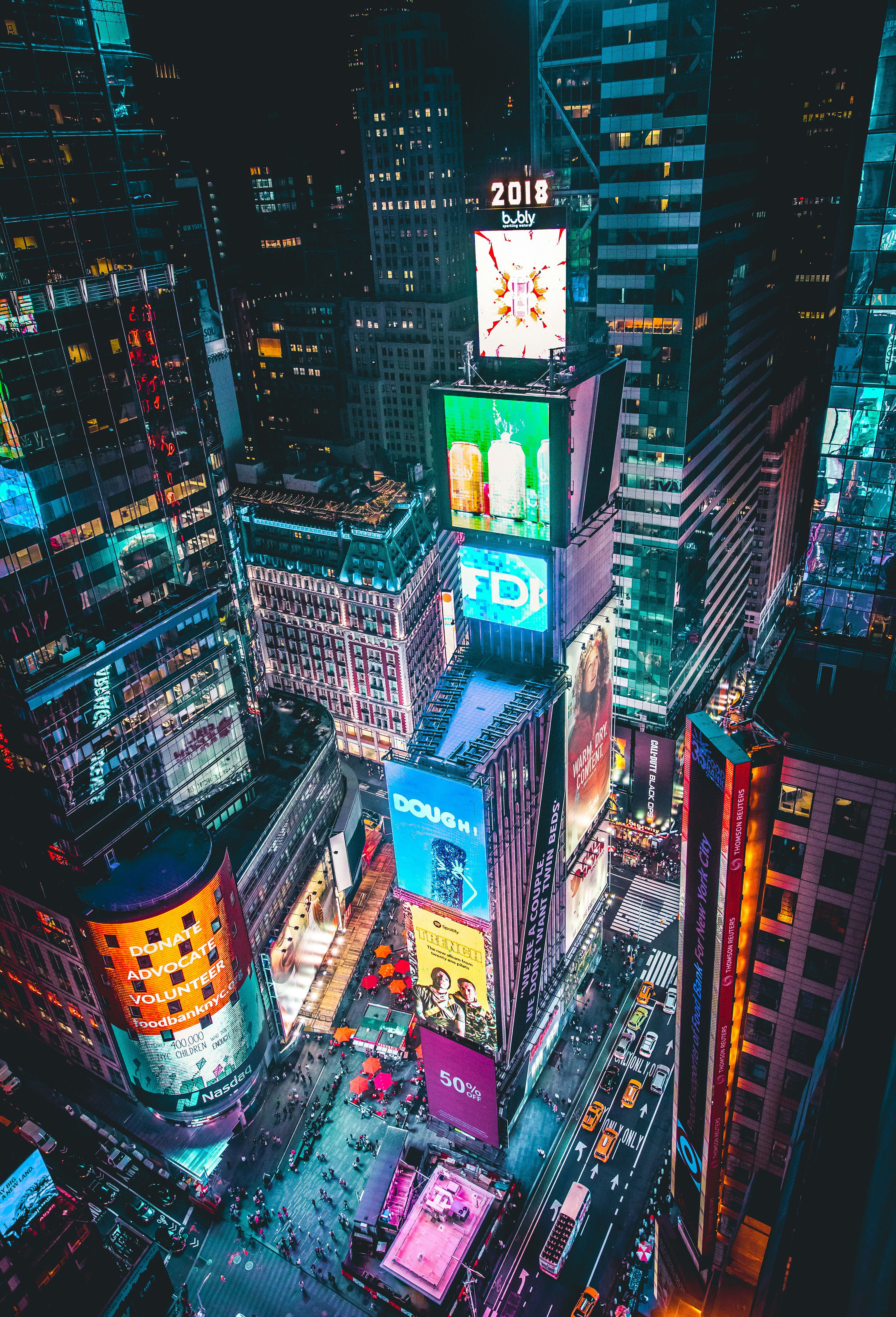 Aerial night view of Times Square, New York City, with brightly lit advertising billboards, busy pedestrian streets, and yellow taxis.