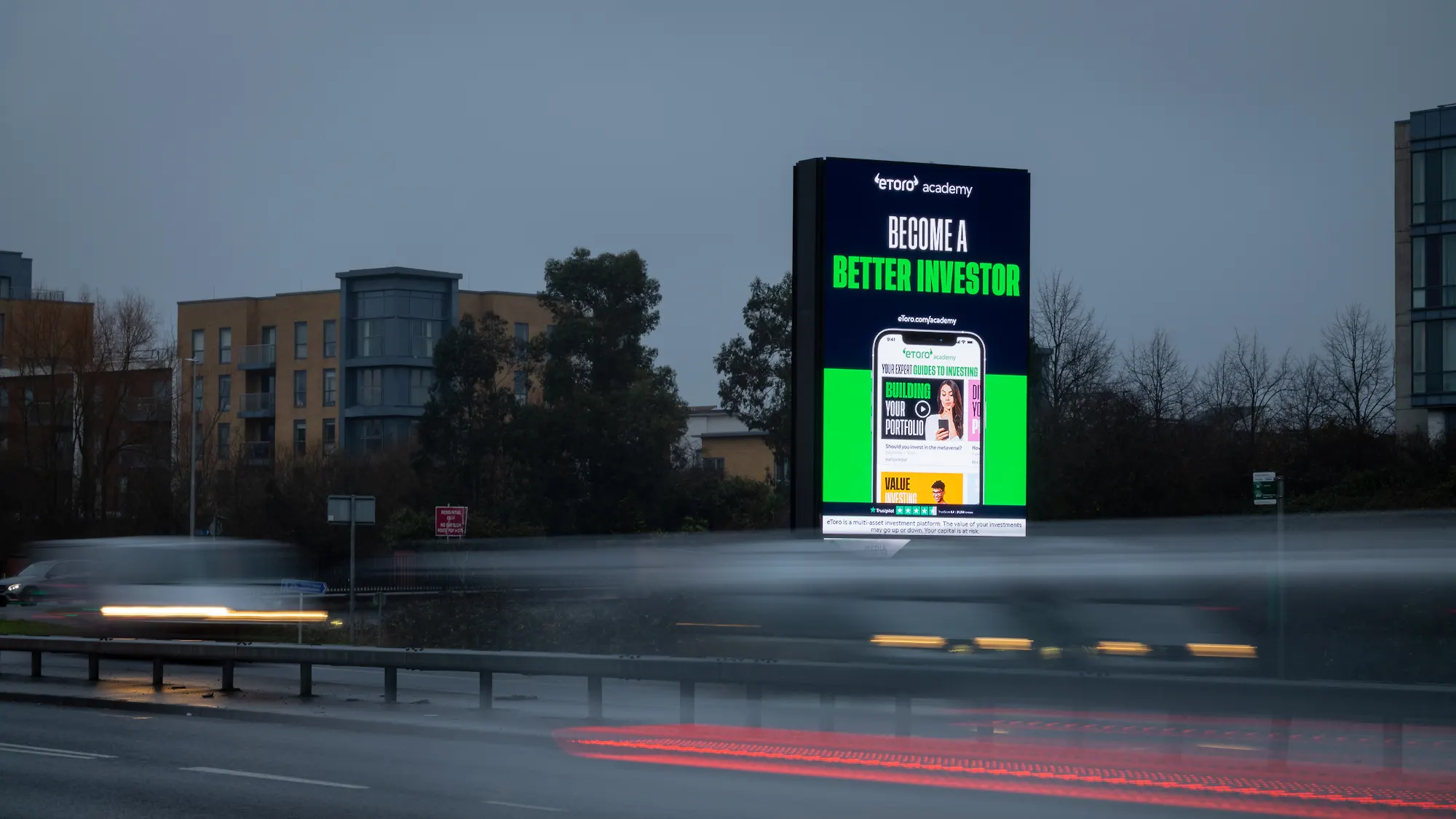 Premium roadside digital billboard at dusk with light-trail traffic, showcasing a live investment platform campaign