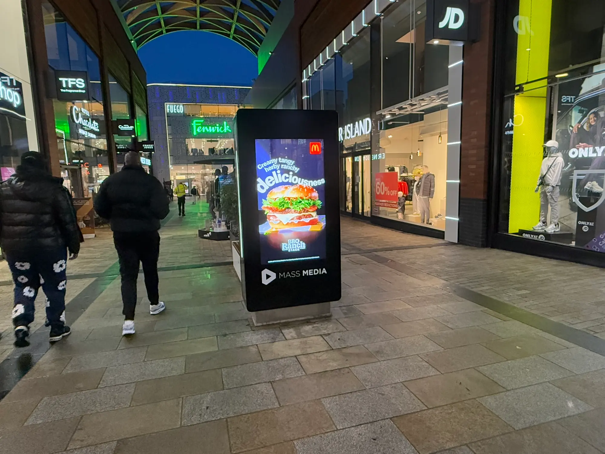 Illuminated digital screen in the Fenwick retail arcade at dusk, showcasing a live advertiser campaign