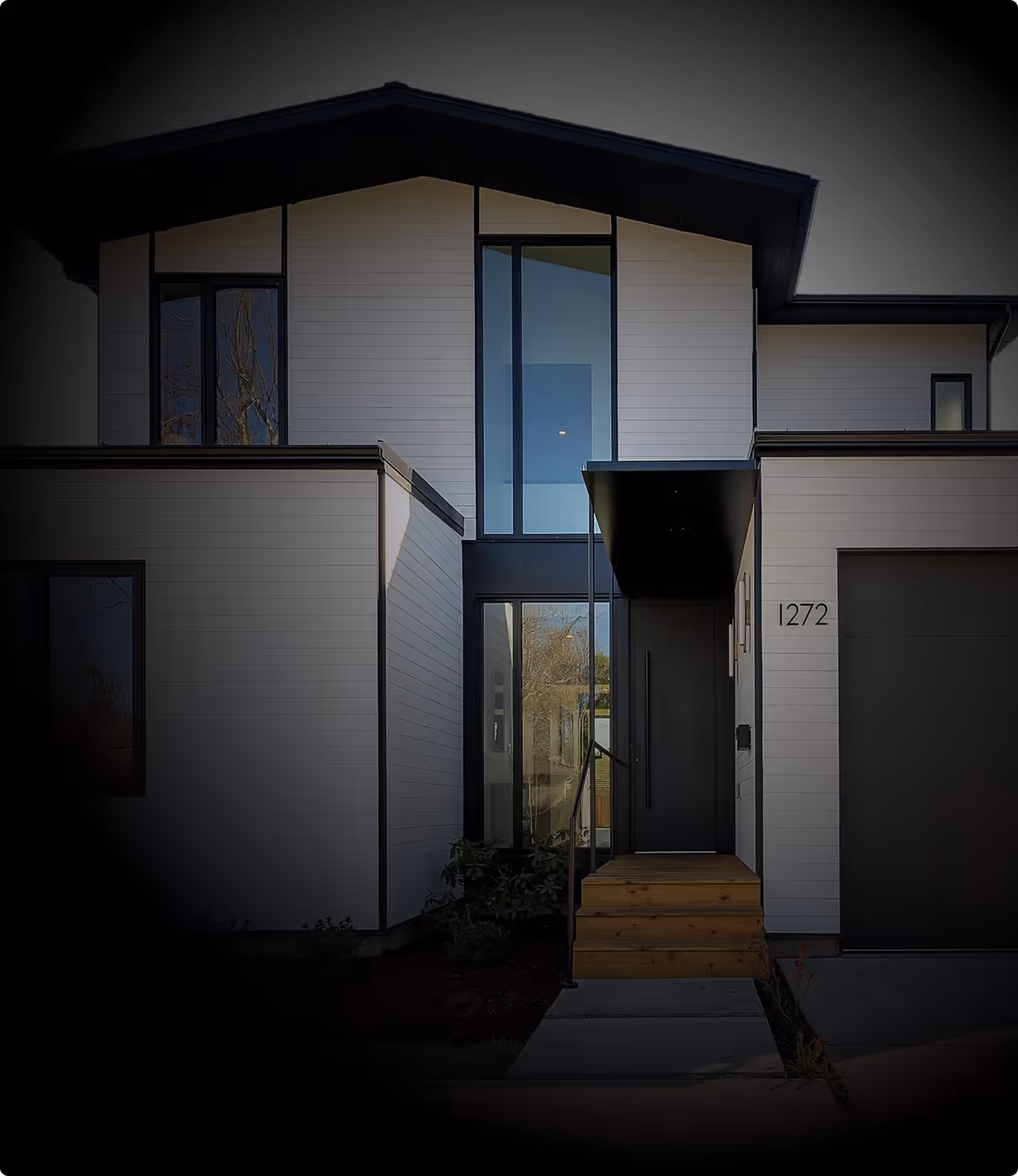 Modern two-story house with white siding, large vertical windows, a black front door under a small awning, and the house number 1272.