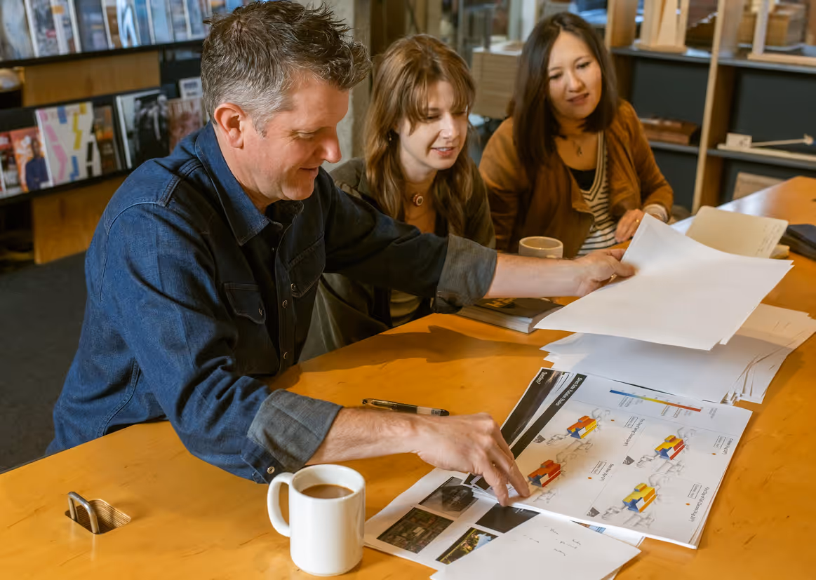 Three people sitting at a table reviewing documents and charts with a coffee cup on the table.