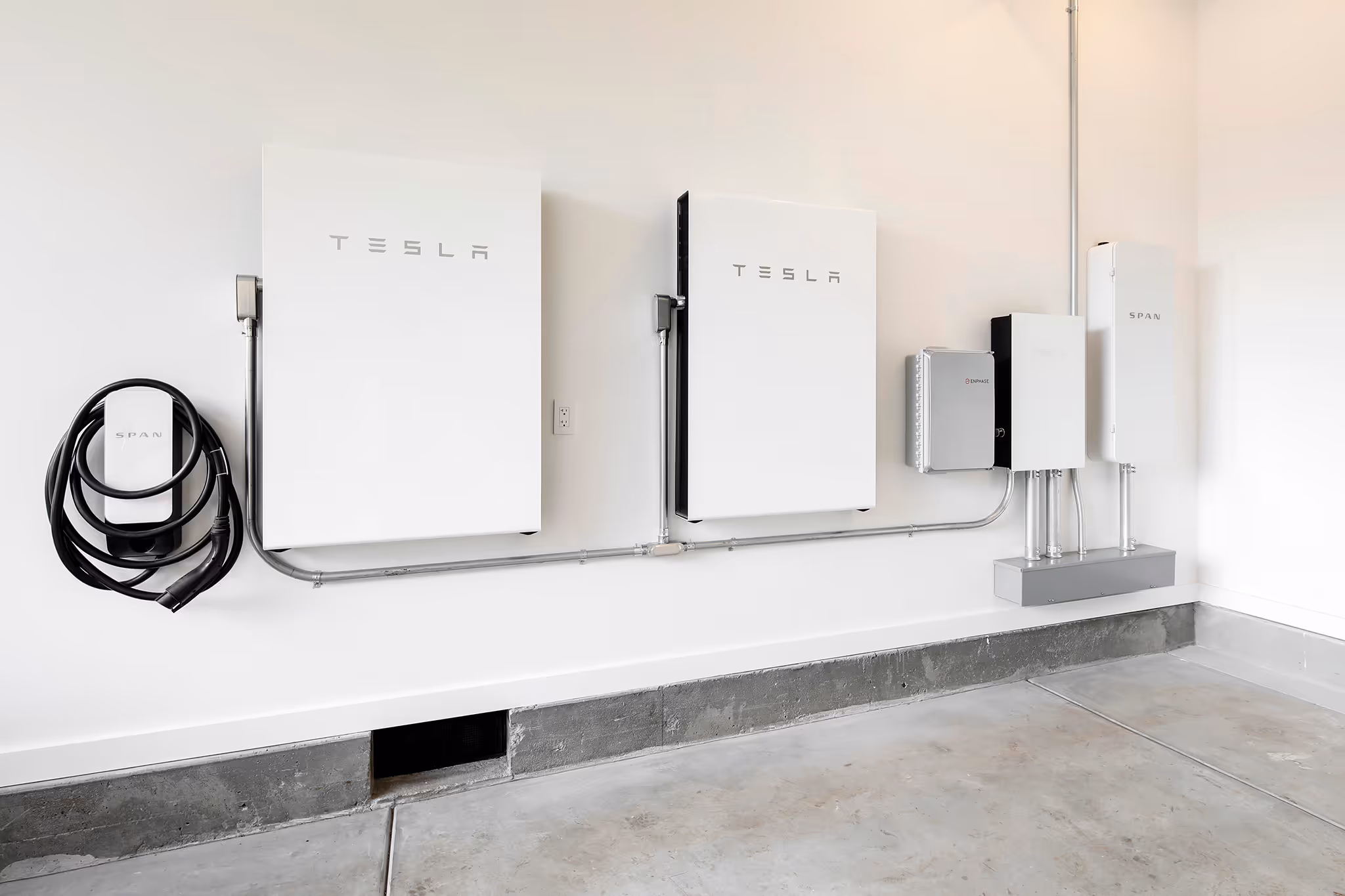 Wall-mounted Tesla Powerwall batteries and Span electrical panels with charging cables in a garage.
