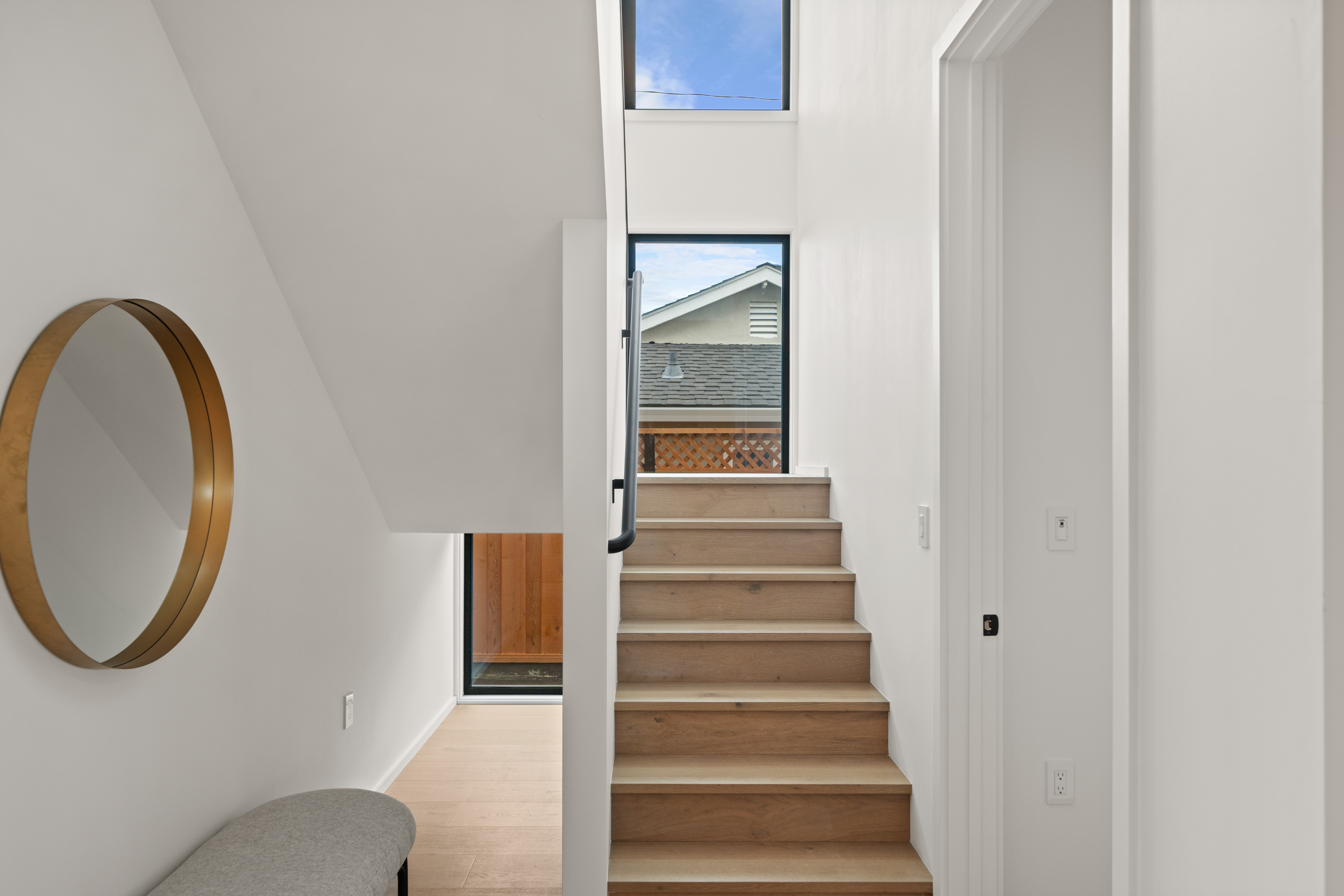 Modern staircase with wood steps, white walls, round mirror, and large window showing rooftop.