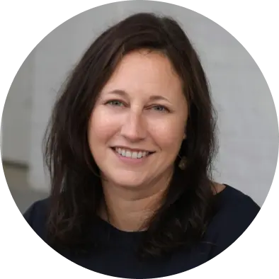 Headshot of a smiling woman with dark, wavy hair, wearing a dark blue top.