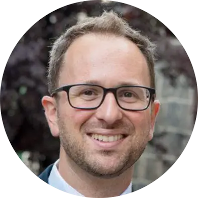 Headshot of a smiling man with short hair and glasses, wearing a white shirt.
