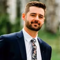 Professional headshot of a man with a beard, wearing a suit and floral tie.