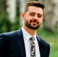 Professional headshot of a man with a beard, wearing a suit and floral tie.