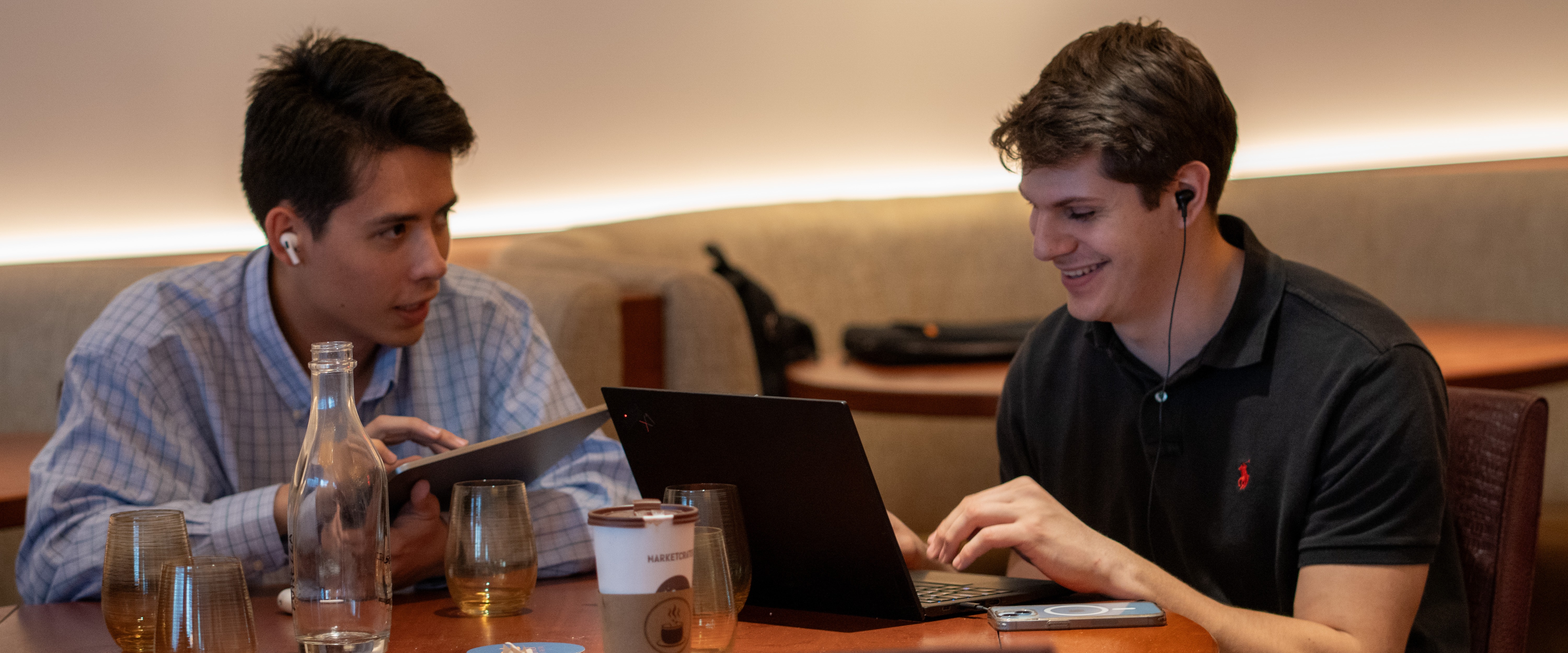 Two TSP scholars, each wearing one earbud, collaborate on a project using their computers at a table.