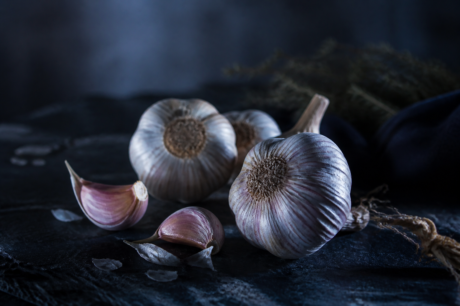 Fresh garlic bulbs and cloves on a dark surface at night