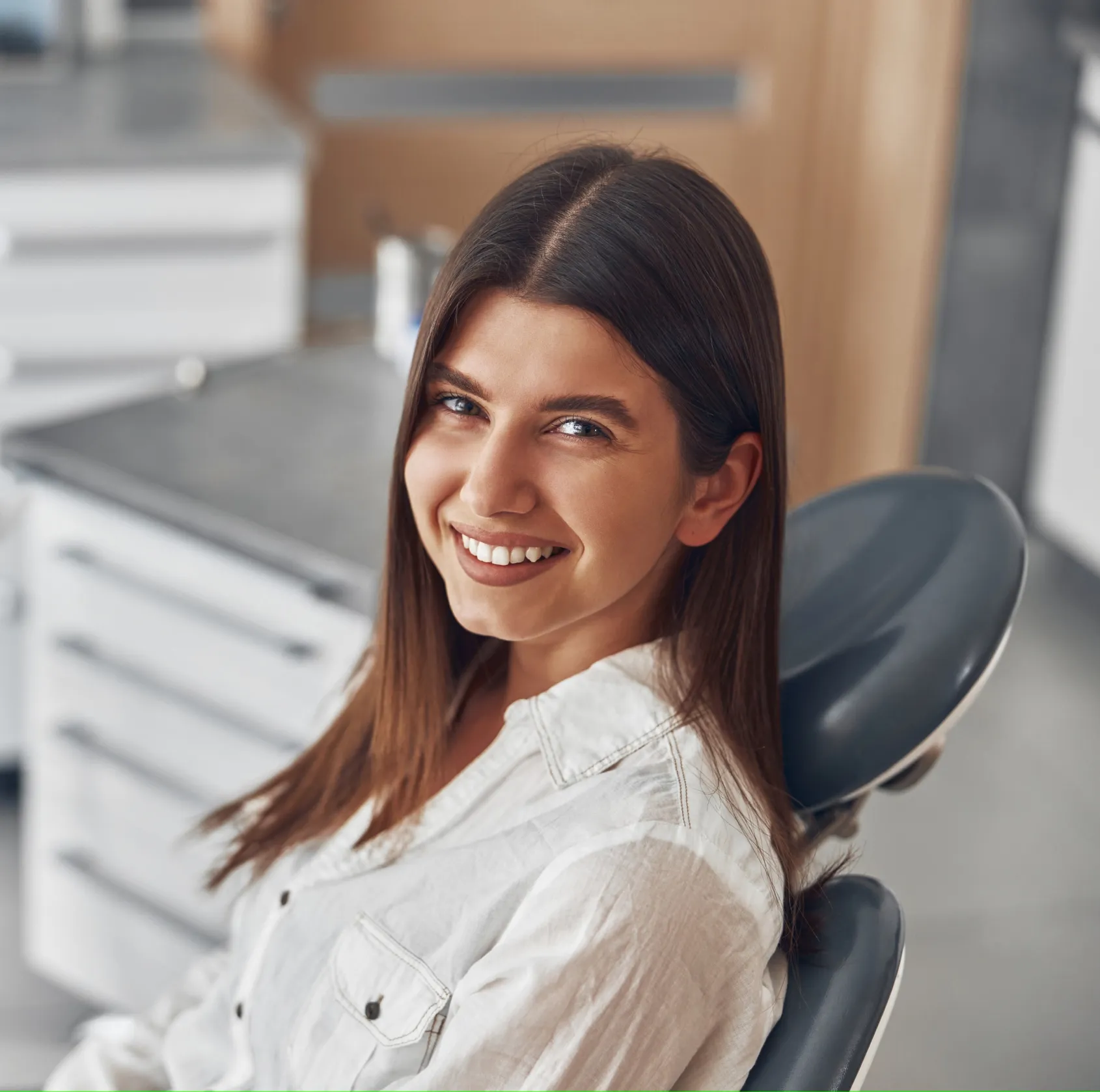 Smiling woman with long brown hair sitting in a dental chair in a clinic.