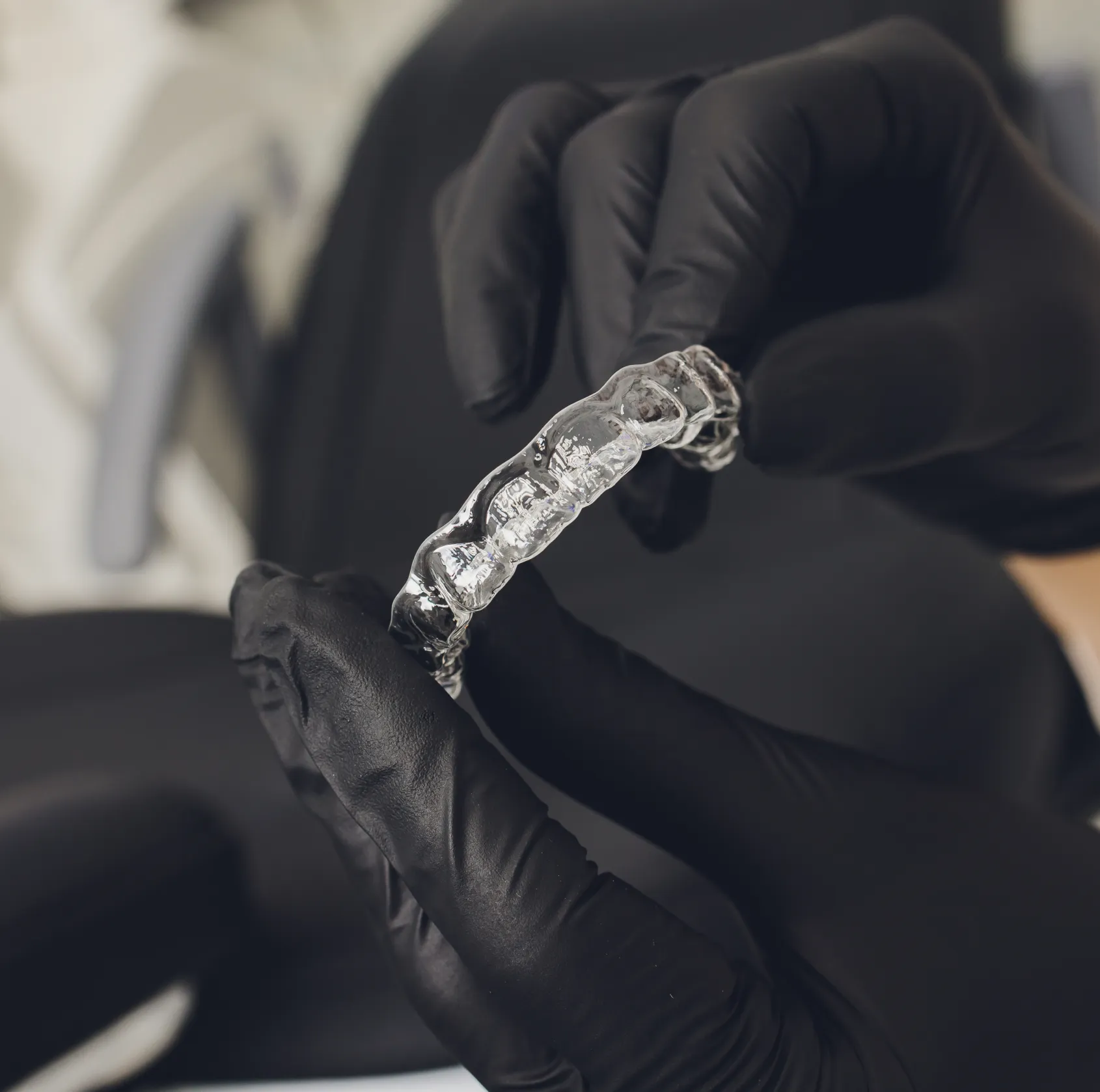 Hands wearing black gloves holding a clear Invisalign dental aligner.