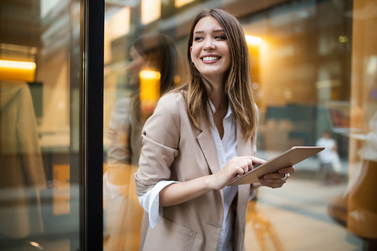 A woman dressed in professional attire smiling as she stands outside holding a tablet.