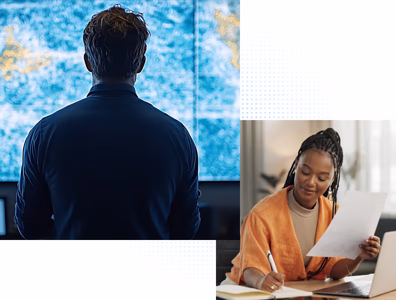 Man looking at a large blue digital screen; woman in orange jacket writing while reviewing a document.