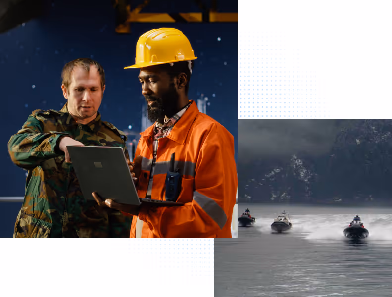 Two men, one in camouflage and one in orange workwear and helmet, checking a laptop together indoors.