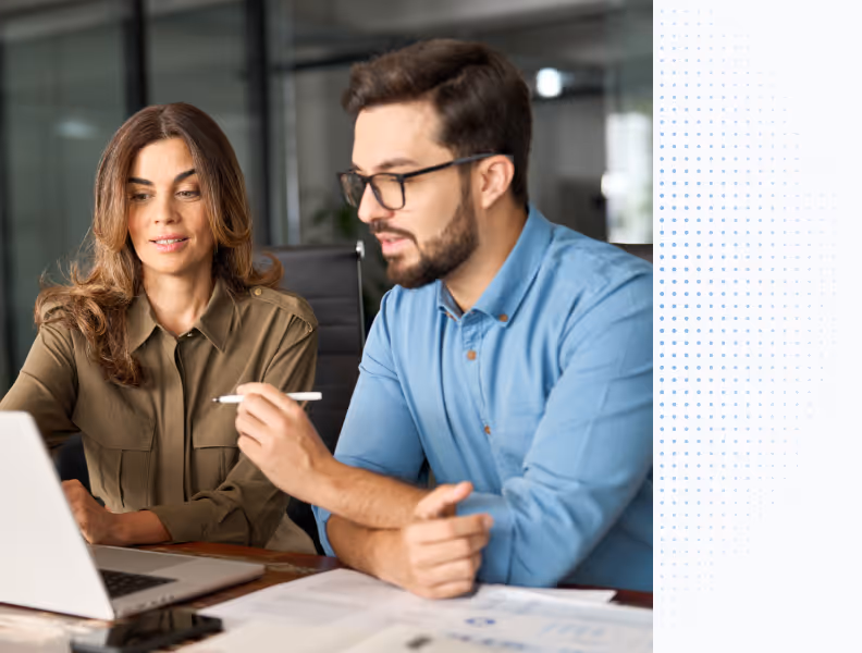 Man and woman sitting at a desk looking at a laptop screen with documents in front of them.